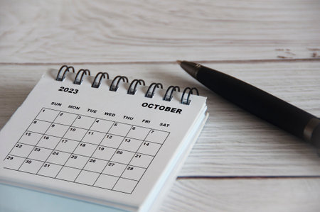 October 2023 white desk calendar with black pen on wooden table. Calendar concept