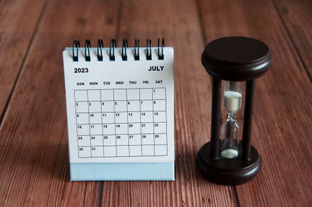 July 2023 white desk calendar with minute glass on wooden table. Calendar conceptの写真素材