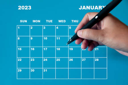 January 2023 calendar with hand holding black pen on blue background. Appointment concept