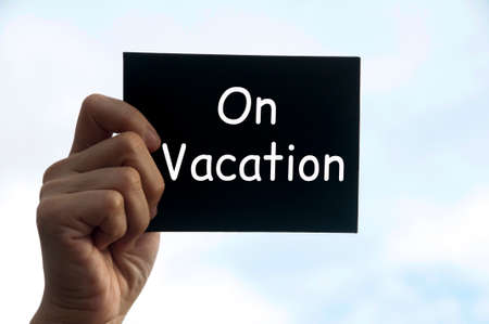 Hand holding black notepad with text - On vacation.