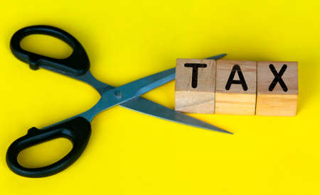 Scissor cutting wooden blocks with text TAX. Cutting tax expenses concept.の写真素材