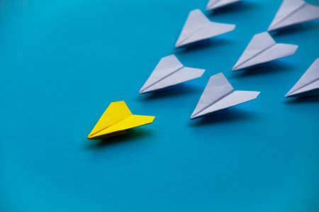 Yellow paper plane origami leading white planes on blue background. Leadership skills concept.の写真素材