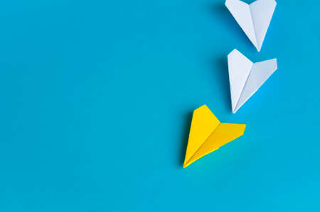 Yellow paper plane origami leading white planes on blue background. Leadership skills concept.