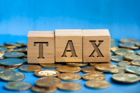 Tax word engraved on wooden block surrounded with gold coins. Taxation concept.の写真素材