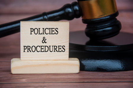 Policies and procedures text engraved on wooden block with gavel background. Policy and procedure concept.の写真素材
