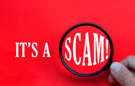 It's a scam text on red cover with hand holding magnifying glass. Scamming and fraud conceptの写真素材