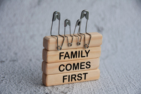 Model safety pin of family sitting on wooden blocks with text - Family comes first. Family concept.の写真素材