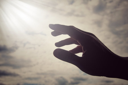 Hand reaching out to bright shining light on sky above. Religious and spiritual concept.の写真素材