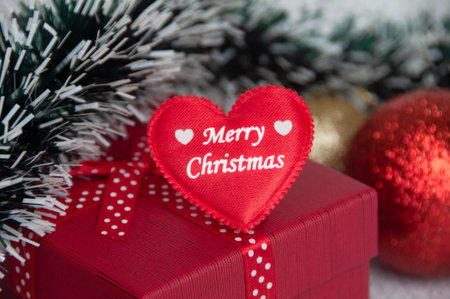 Merry Christmas text on heart shape on top of red color present with Christmas decoration background. Christmas gift and celebration concept.の写真素材