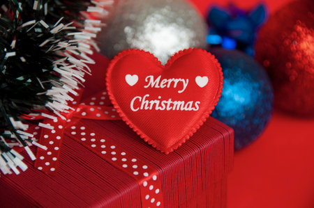 Merry Christmas text on heart shape on top of red color present with Christmas decoration background. Christmas gift and copy space concept.の写真素材