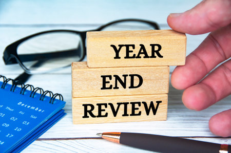 Year end review text on wooden blocks with December calendar, glasses and pen. Accounting and year...