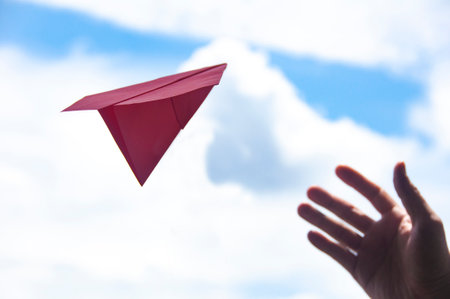 Hand trying to catch flying red paper plane. Travelling and vacation concept.の写真素材