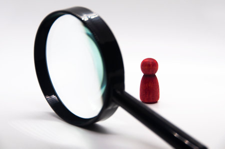 Red wooden figure looking through a magnifying glass with white background.の写真素材