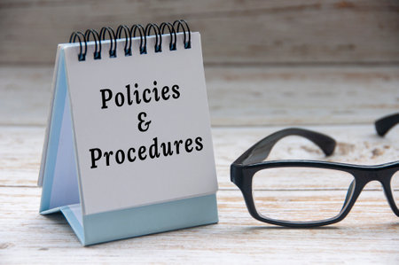 Policies and procedures text on notepad with glasses on white wooden cover background