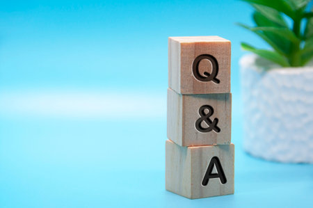 Q and A text engraved on wooden blocks with light blue and table plant background. Question and answer concept. Copy spaceの写真素材