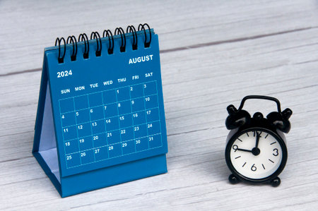 August 2024 calendar on wooden desk and alarm clock with customizable space for text. Monthly calendar concept and copy spaceの写真素材