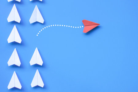 Top view of red paper airplane origami leaving other white airplanes on blue background with customizable space for text or ideas. Leadership skills concept and copy space.の写真素材