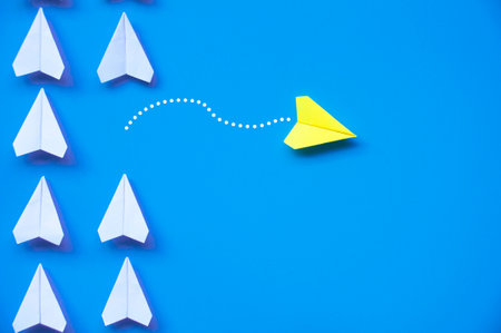 Yellow paper airplane origami leaving other white airplanes on blue background with customizable space for text or ideas. Leadership skills concept and copy space.の写真素材