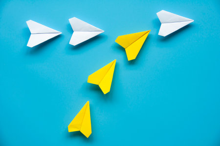 Yellow paper airplane origami joining other white airplanes on blue background with customizable space for text or ideas. Leadership concept.の写真素材