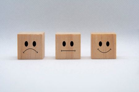 Sad, neutral and happy emoticon faces on wooden cubes with white background cover. Customer...