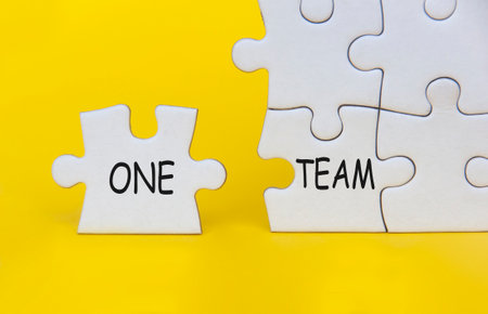 One Team text on separated jigsaw puzzle on yellow background. Teamwork concept.の写真素材