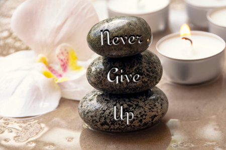 Never give up text engraved on black zen stones with orchid and candle background.の写真素材
