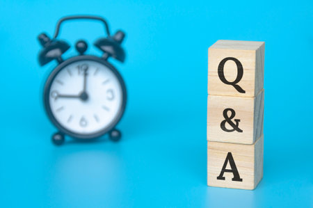 Q and A text on wooden blocks with light blue and alarm clock background. Question and answer concept. Copy space.の写真素材