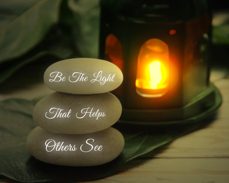 Motivational and inspirational quote on Zen stones - Be the light that helps others see text with antique lamp background.の写真素材