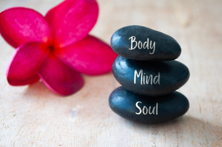 Body, Mind and Soul text engraved on black zen stones with red flower. Meditation and spa concept.の写真素材
