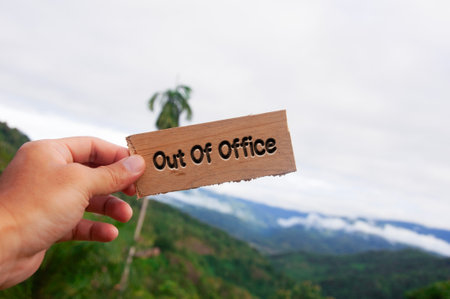 Hand holding wooden block with out of office text on beautiful nature background.の写真素材