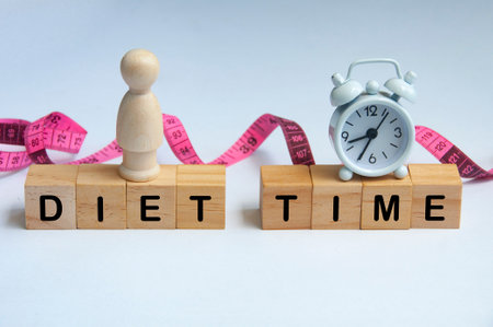 Diet time text on wooden cube with alarm clock and wooden figure with measuring tape background.の写真素材