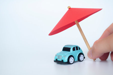 Toy car covered with toy umbrella representing car insurance concept.の写真素材
