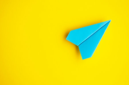 Top view of blue paper airplane with customizable space for text on yellow cover background.の写真素材