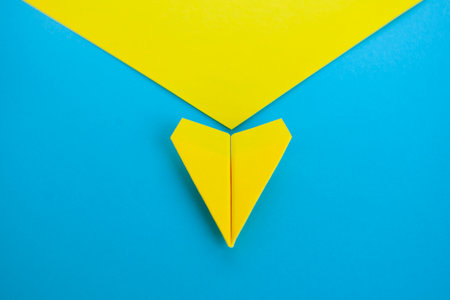 Close up top view view of yellow paper airplane flying along the route on blue background.