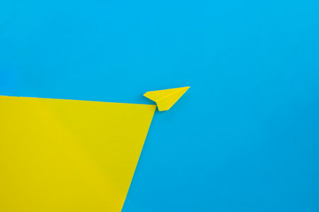 Angle view of yellow paper airplane flying along the route on blue background.