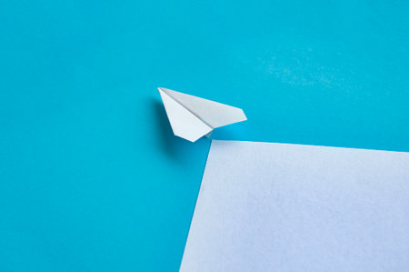Angle view of paper airplane flying on blue background with customizable space for text.の写真素材