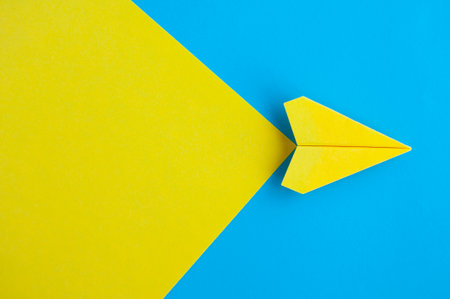 Top view of yellow paper airplane flying on blue background with customizable space for text.
