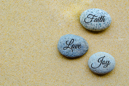 Top view of Faith, Love and Joy text engraved on stones with beach sand background.の写真素材