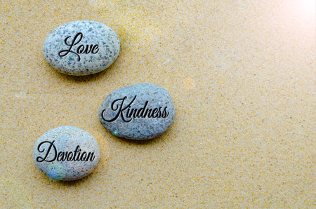 Top view of Love, Kindness and Devotion text engraved on stones with beach sand background.の写真素材