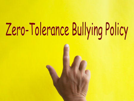Hand pointing at Zero Tolerance Bullying Policy text written on yellow cover. Safe workplace concept.の写真素材