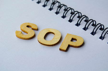 Top view of SOP wooden letters on white notepad. Standard Operating Procedure concept.の写真素材