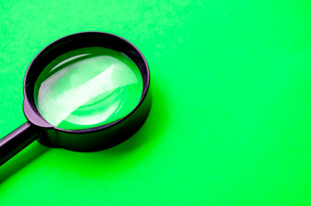 Magnifying glass on green cover background with customizable space for text or ideas.の写真素材