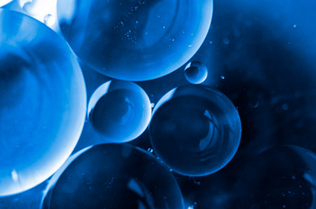 Close-up of oil swirling on water, reflecting a subtle gradient background.の写真素材