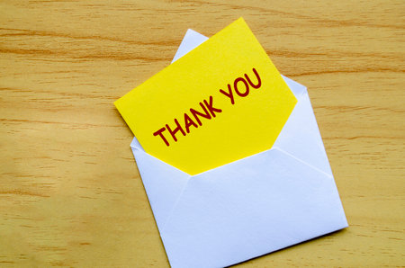 White envelope on a wooden surface with a yellow card partially pulled out with Thank You textの写真素材