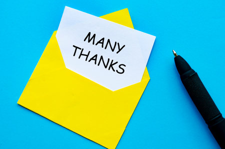 Yellow envelope on a blue cover with a white card partially pulled out with Many Thanks textの写真素材
