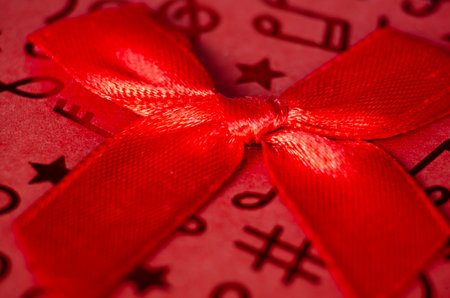 Close up of red gift ribbon with white polka dots tied into a bow, placed on a textured red and pink striped backgroundの写真素材