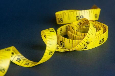 Close up view of yellow measure tape on dark background with customizable space for text.