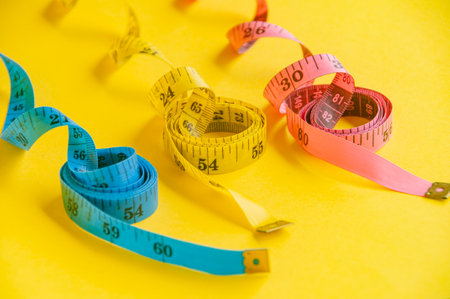 Precision and creativity symbolized by a blue, yellow and pink tape measure on yellow canvas.