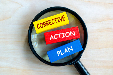 Corrective Action Plan text on colored wooden blocks with magnifying glass as background. Root cause analysis concept.の写真素材