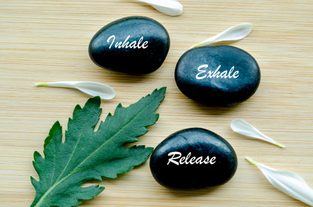 Inhale, Exhale and Release text on zen stones surrounded by flower petals. Inner peace concept